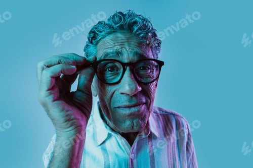 Preview: Senior man posing in studio under colored gel lights.