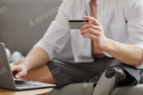 Preview: Man with prosthetic leg entering credit card information online using laptop