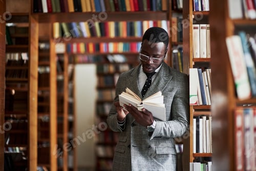 Preview: An African American man in a business suit standing in a library in the reading room
