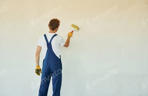 Preview: Clean walls. Young man working in uniform at construction at daytime