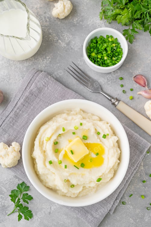 Preview: Cauliflower puree with butter and green onions in a white bowl. Healthy food. Copy space.