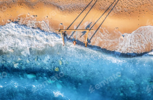 Preview: Aerial view of woman on the swing, beautiful blue sea with waves