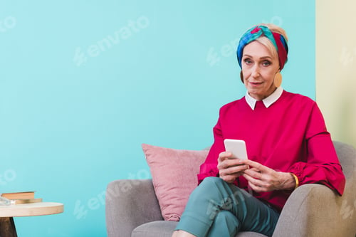 Preview: senior woman using smartphone while sitting in armchair
