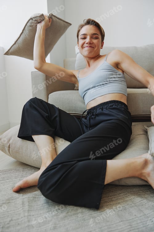 Preview: Teenage girl smile everyone sits at home near the couch and tosses up pillows, fun game and