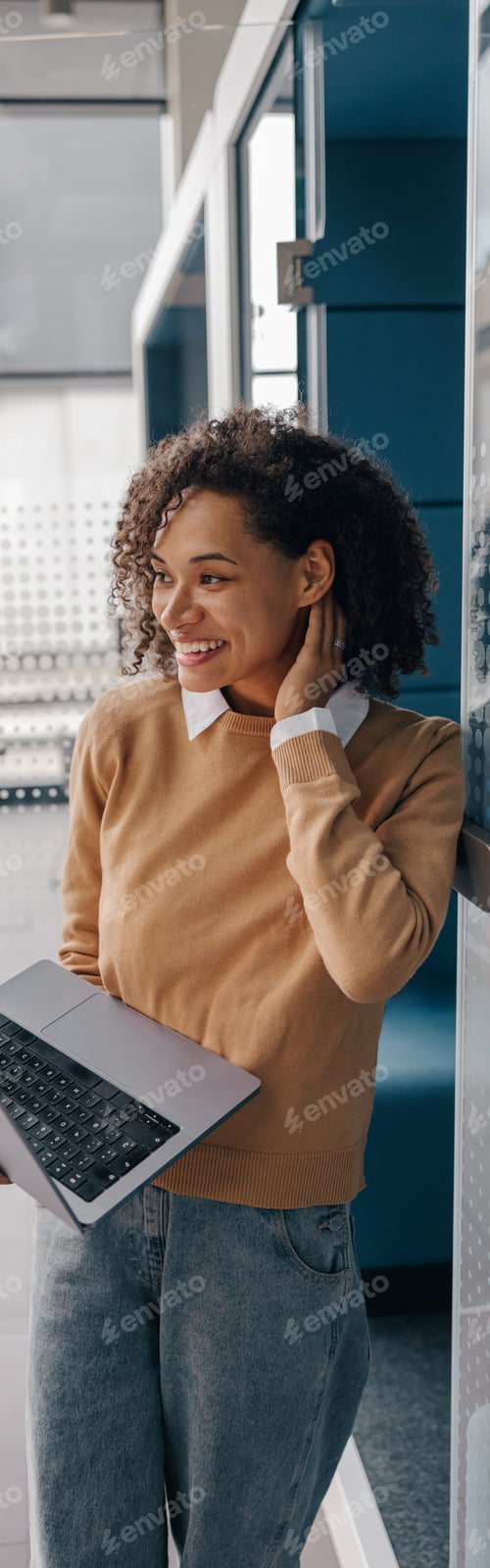Preview: Young smiling female manager using laptop while standing on modern office background