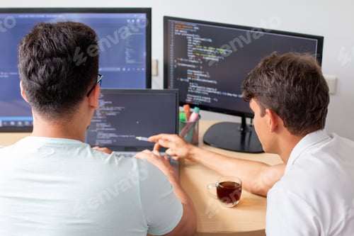 Preview: Two young programmers work on a programming project on a modern desktop computer with three monitors
