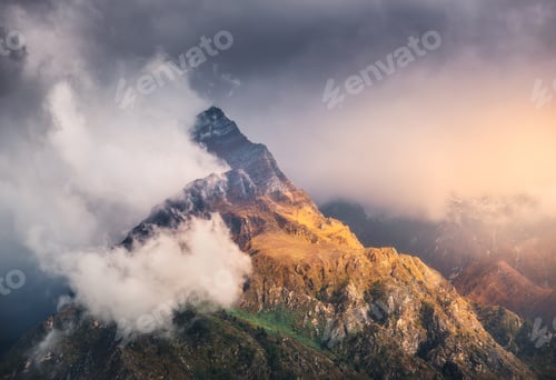 Preview: Mountain peak in low clouds at colorful sunset in Nepal