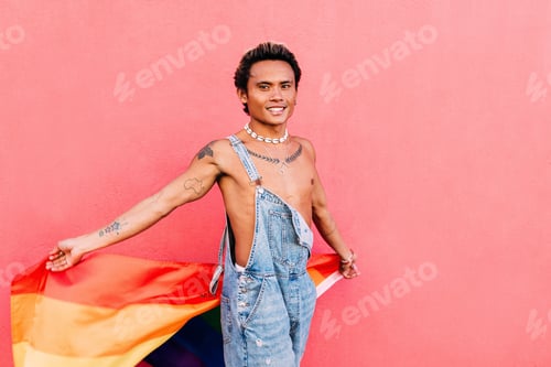 Preview: Young guy in denim overalls holding a rainbow flag outdoors