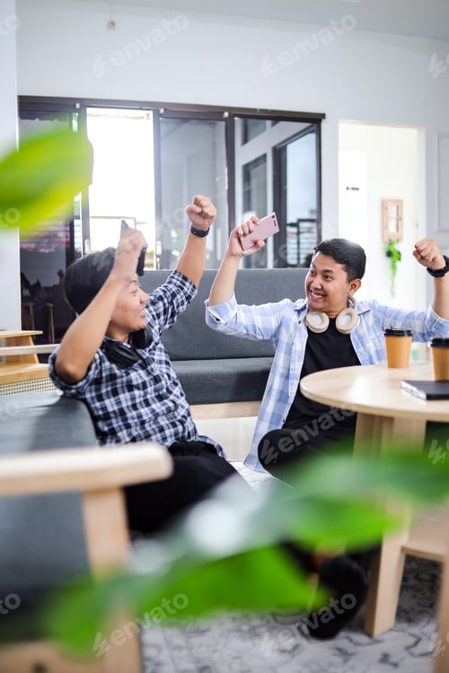 Preview: Cheerful Two Young Asian Workers Celebrate Victory With Smartphone After Playing Mobile Games