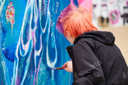 Preview: Young woman painter painting multicolored picture on large canvas, outdoor art performance festival
