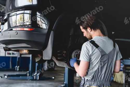 Preview: Mechanic fixing repairing tires wheels of automobile car at vehicle station MOT service in grey robe
