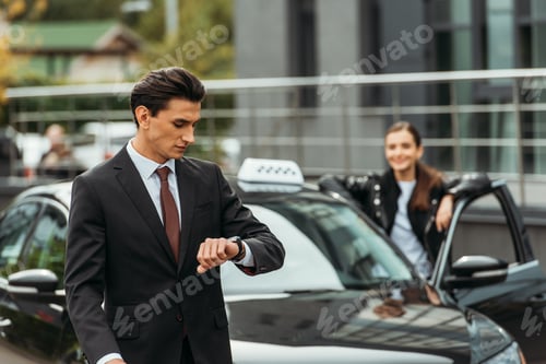 Preview: Selective focus of businessman looking at wristwatch and taxi driver by car