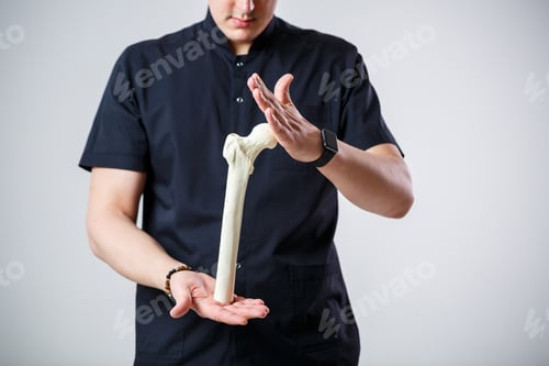 Preview: Young male doctor chief physician in a black surgical suit. Close-up portrait. Holds a femur