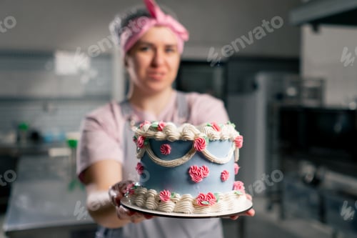 Preview: in a professional kitchen a female baker stands with a finished cake in her hands she smiling