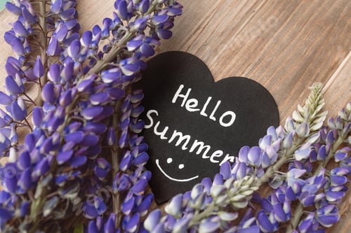 Preview: hello summer lettering with smile on black wooden heart fresh lupine flowers on brown wooden table