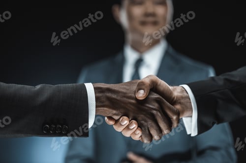 Preview: selective focus of multiethnic business partners shaking hands with colleague standing near by