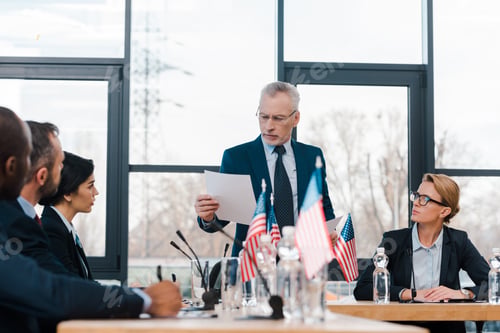 Preview: selective focus of bearded businessman holding paper near multicultural diplomats and american flags