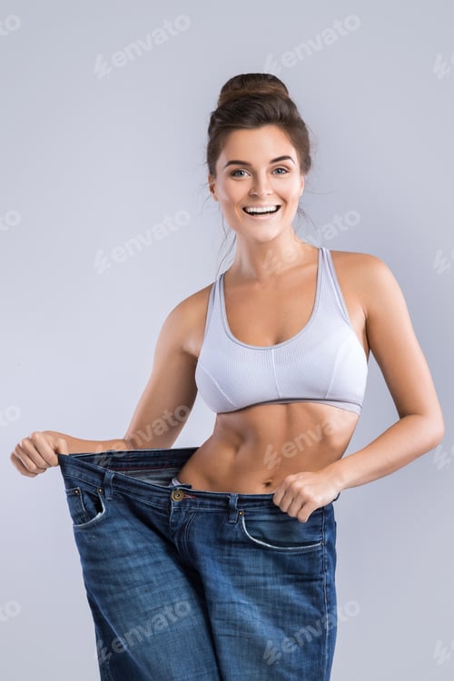 Preview: Happy woman wearing jeans after weight-loss on gray background
