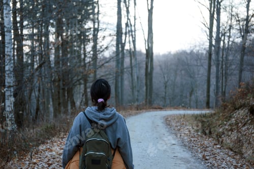 Preview: Rear view of young woman hiking on path through forest with bare trees in winter