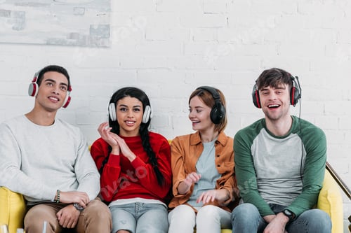 Preview: multicultural listening music with headphones while sitting on yellow sofa
