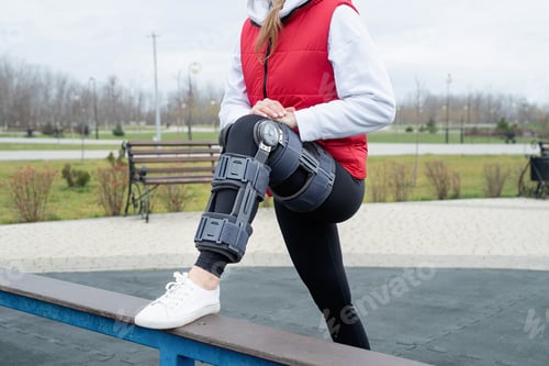 Preview: Woman wearing knee brace or orthosis after leg surgery working out in the park
