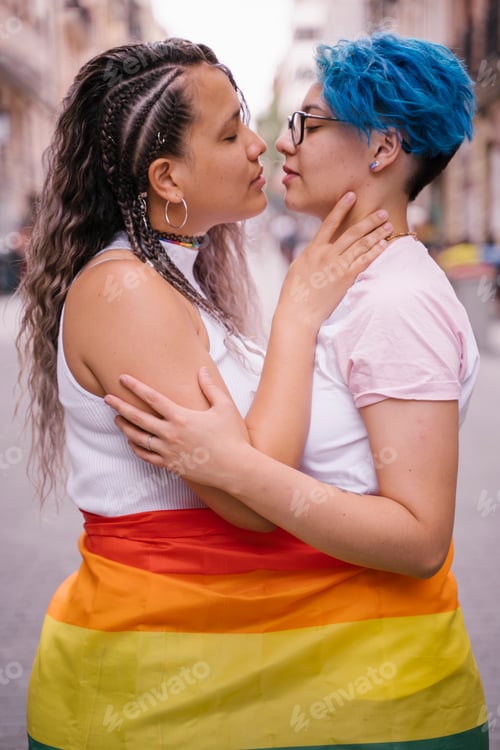 Preview: lesbian couple wearing with pride a lgbt flag and kissing on the street.