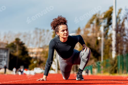 Preview: Young woman stretching her muscles before running on sport track outdoors.