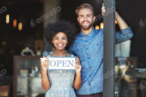 Preview: Portrait of two proud coffee shop owners holding up a sign on opening day