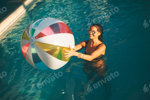 Preview: Young woman with ball in the pool at sunny day