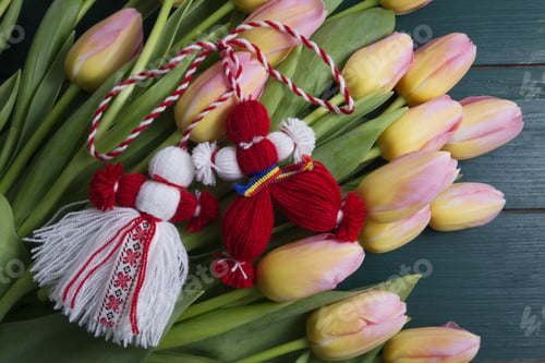 Preview: Martenitsa, Martisor on a bouquet of pink tulips on a green wooden table top view