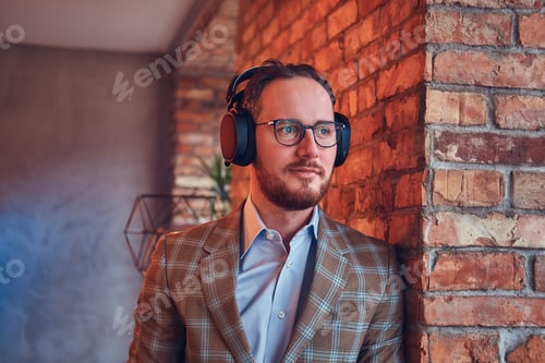 Preview: Close-up portrait of a stylish man in a flannel suit and glasses listening music.