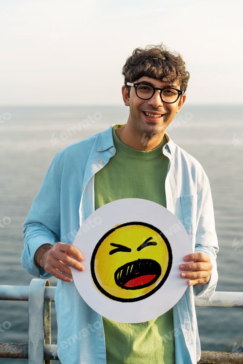 Preview: Happy young man wearing eyeglasses holding yellow amazed emoji face