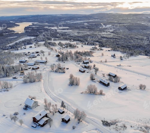 Preview: High angle shot of a town covered in the snow surrounded by forests and a lake under a cloudy sky