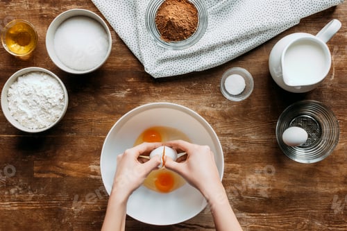 Preview: cropped shot of woman breaking eggs into bowl for pastry on wooden table