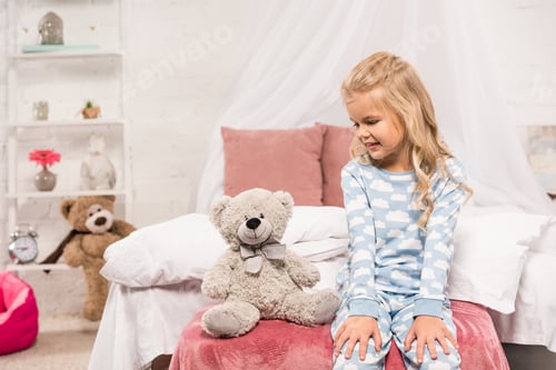 Preview: smiling cute kid sitting on bed with teddy bear
