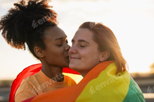 Preview: Happy lesbian couple having tender moment at sunset during LGBT pride parade outdoor