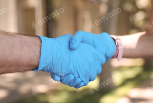 Preview: Man and woman in protective gloves shaking hands to say hello outdoors, closeup