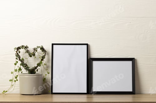 Preview: Black empty frames with copy space and heart shape plant on table against white wall