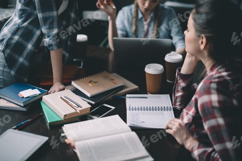 Preview: Concentrated girls students drinking coffee and studying together at table