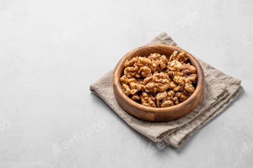 Preview: Walnut in a wooden bowl on a linen napkin on a light textured background.