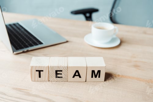 Preview: selective focus of team lettering on wooden cubes near laptop and cup with coffee