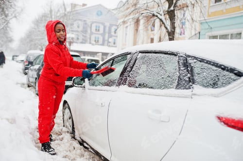 Preview: African american woman in red hoodie clean car from snow in winter day.