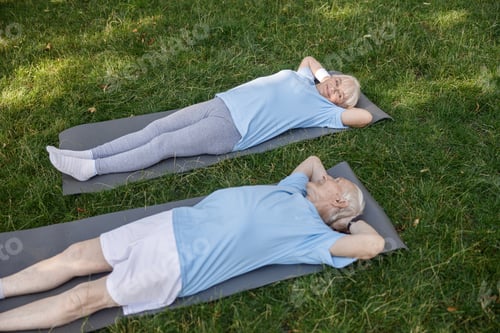 Preview: Lovely senior family couple looks at each other lying on mats after training in green park