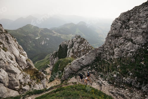 Preview: People striding on a narrow path that ascends towards a mountain range in the distance