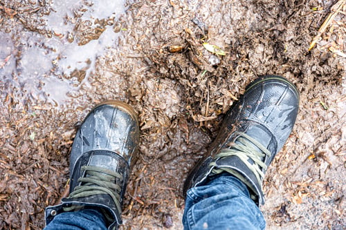 Preview: View from above on pair of trekking shoes in a mud.