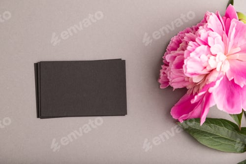 Preview: Black business card with pink peony flowers on gray pastel background. top view, copy space.