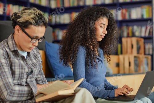 Preview: Young Asian Man Reading Book Beside Young Black Woman Using Laptop