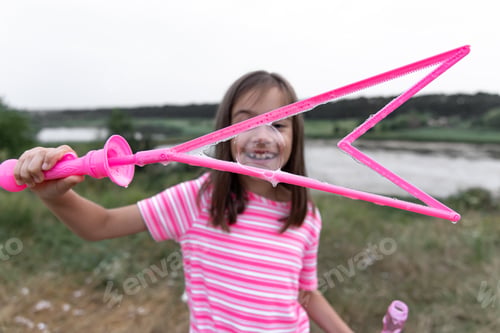 Preview: A little girl blows large, colorful soap bubbles in the nature.