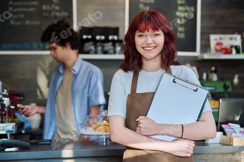 Preview: Portrait of young female waitress in front of counter in coffee shop