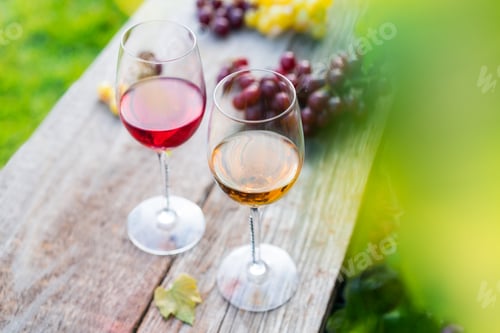 Preview: Glasses with white and red wine and grape berries on the wooden table in the vineyards, winery